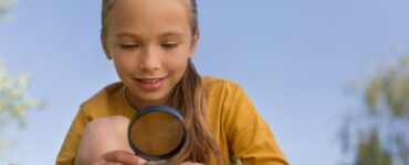 bambina che osserva una foglia con una lente nella mano