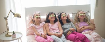 Quattro bambine in pigiama con fette di cetrioli sugli occhi sedute sul letto